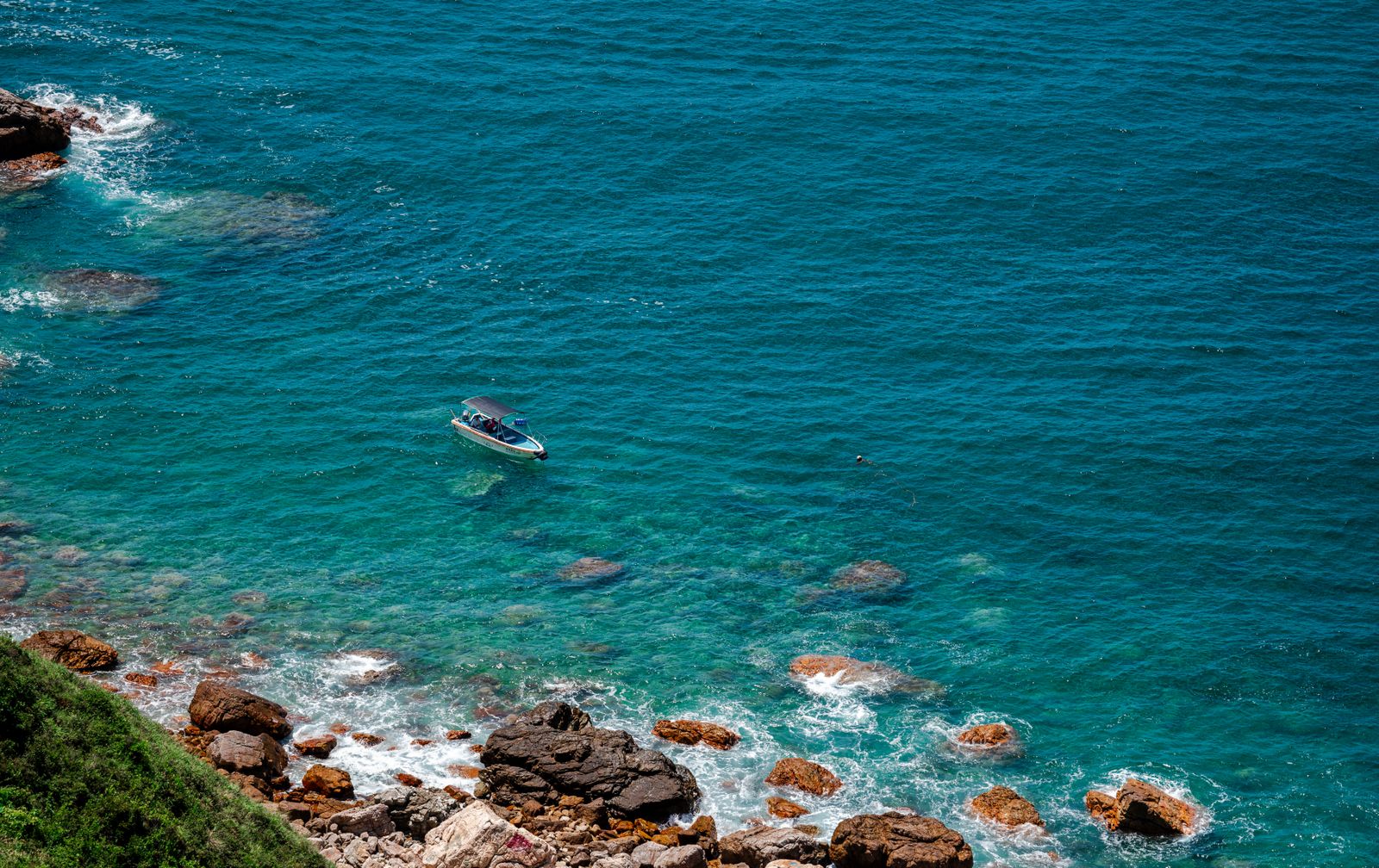 Un petit bateau sur une mer turquoise au pied d’une côte rocheuse, photographie d’ambiance